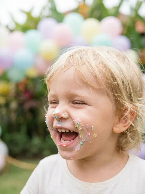 Toddler girl giggling with birthday cake frosting on her face at a Bali party